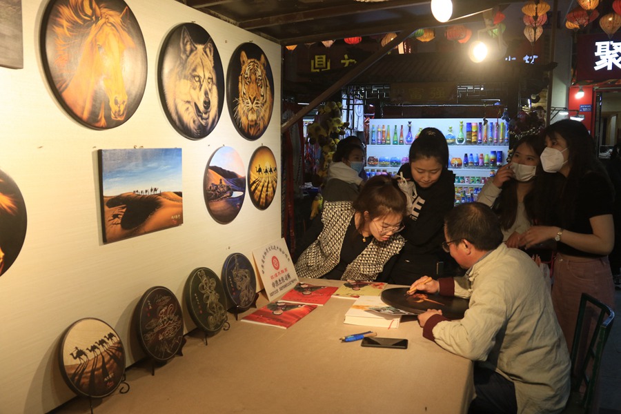 游客在敦煌夜市欣賞選購木雕畫。張曉亮攝