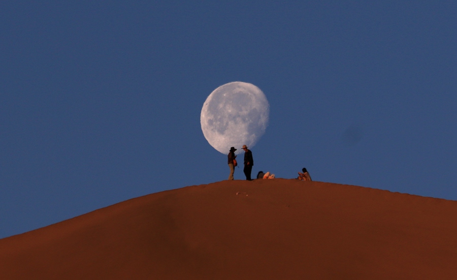 6月7日清晨，游客在甘肅省敦煌市鳴沙山山頂賞月。張曉亮攝