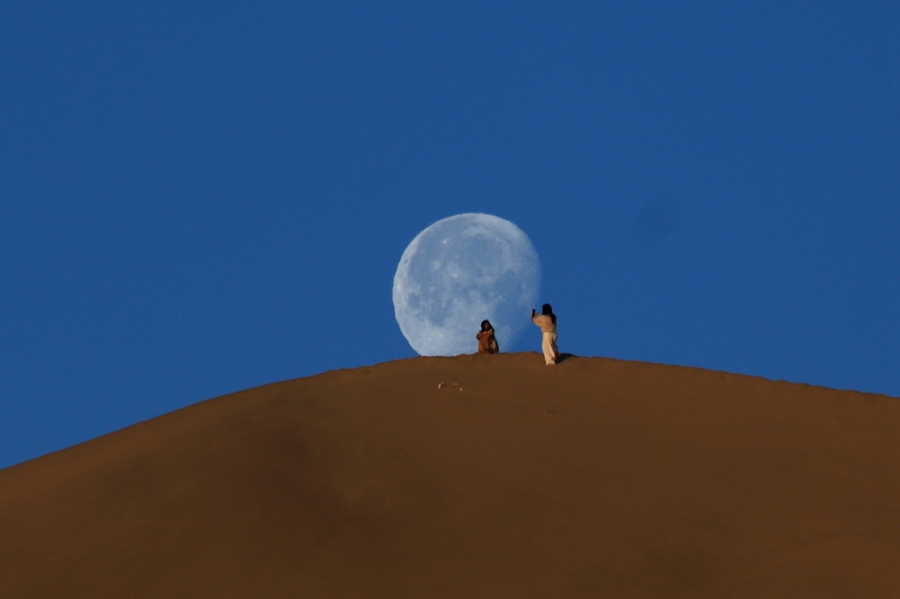 6月7日清晨，游客在甘肃省敦煌市鸣沙山山顶赏月。张晓亮摄