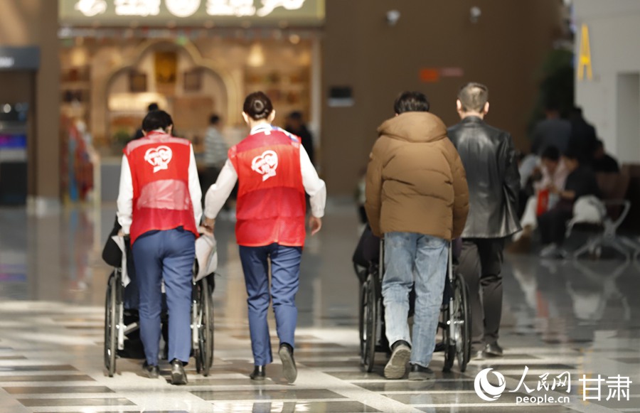 兰州中川国际机场“小红帮您”工作人员护送老年旅客登机。人民网记者 焦隆摄